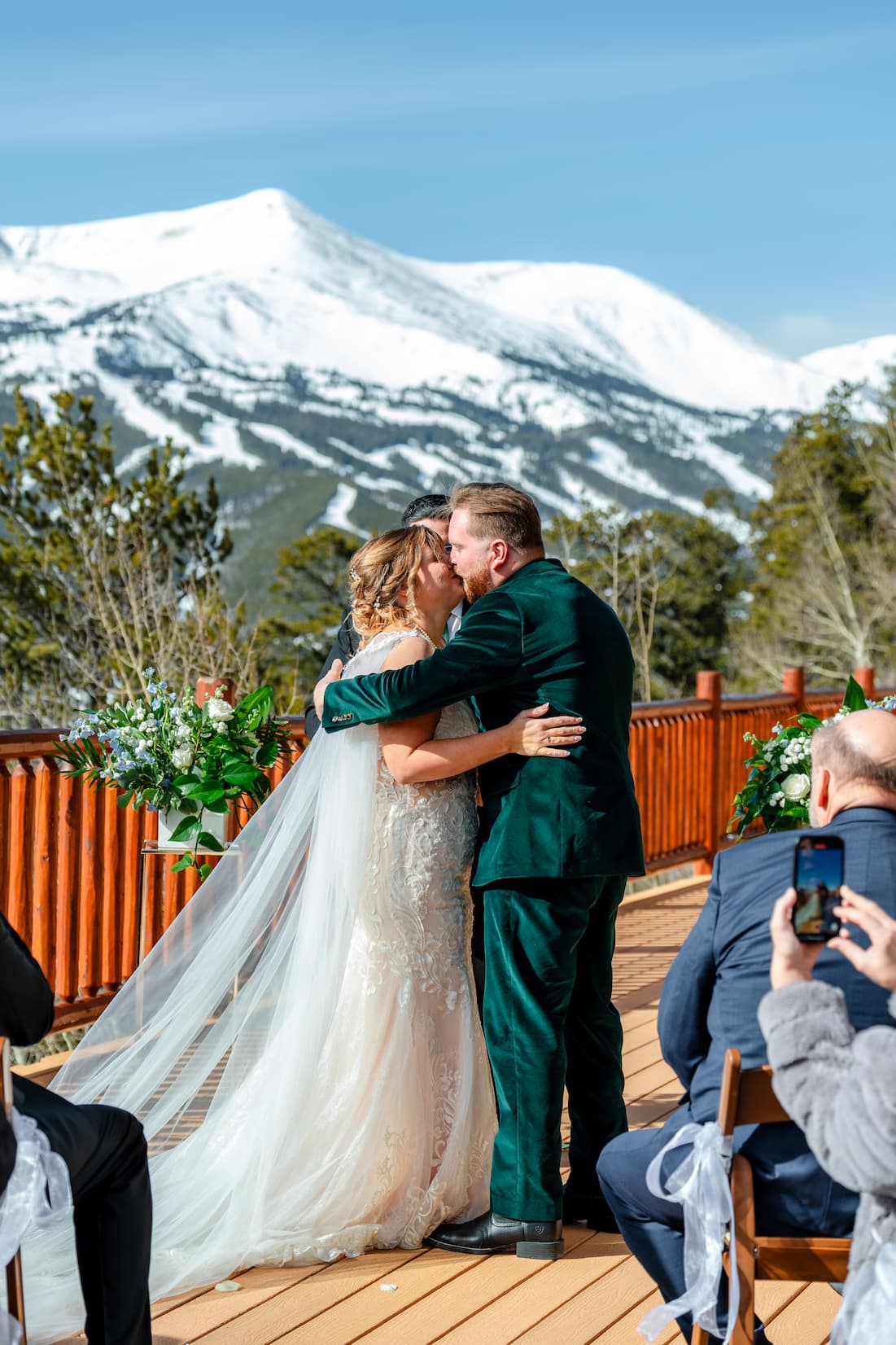Pricing A bride and groom sharing their first kiss during an outdoor mountain wedding ceremony, featuring a spectacular view of snow-capped mountains.